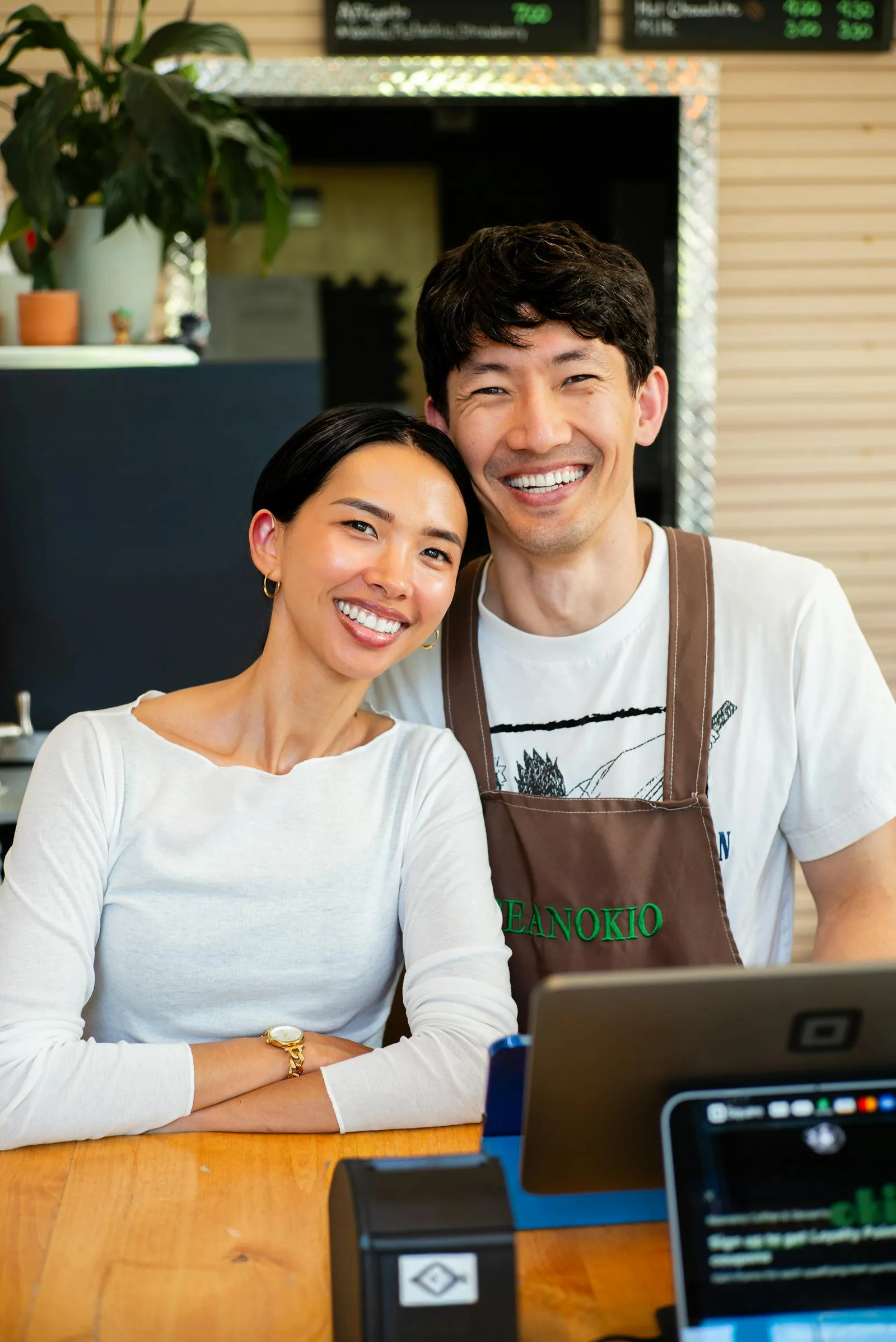 Two smiling baristas behind the counter of a cozy coffee shop.