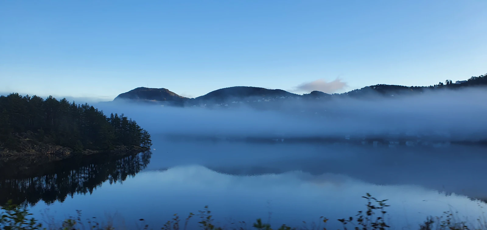 Misty mountains reflected in a calm lake at dawn.